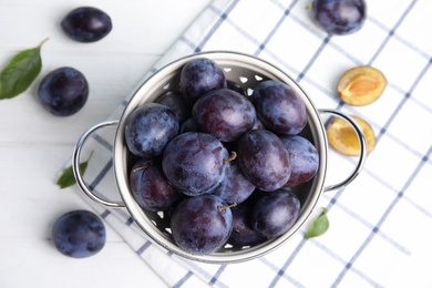 Delicious ripe plums in colander on white table, flat lay