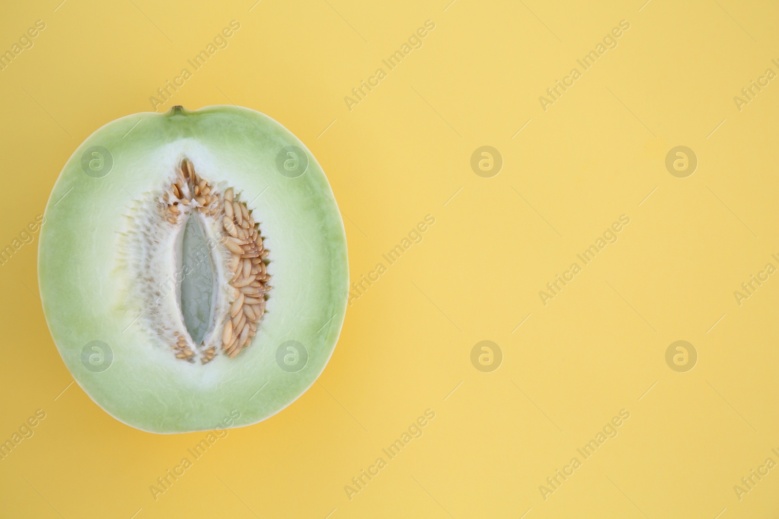 Photo of Half of fresh ripe honeydew melon on yellow background, top view. Space for text