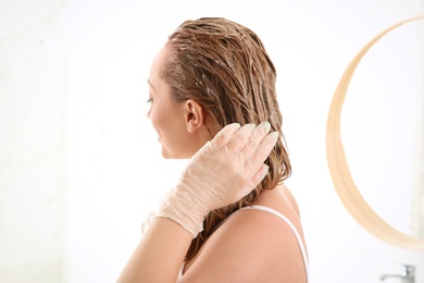 Photo of Young woman dyeing her hair in bathroom