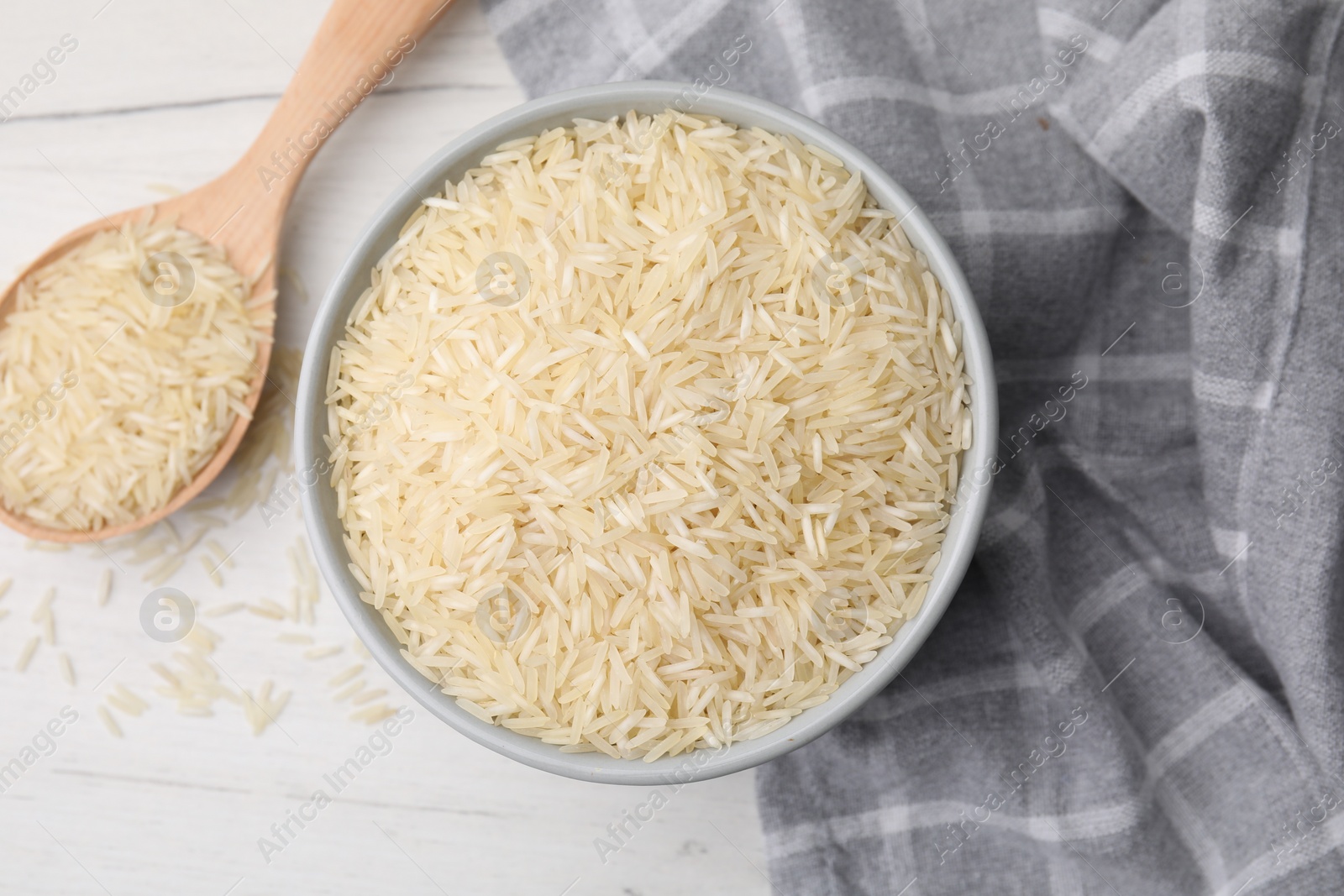 Photo of Bowl and spoon with raw rice on white wooden table, flat lay