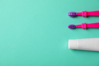 Baby toothbrushes and toothpaste with space for text on color background, top view