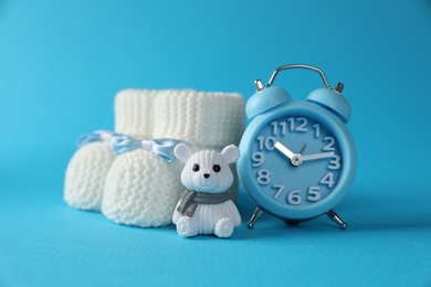Photo of Alarm clock, toy bear and baby booties on light blue background. Time to give birth