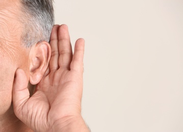 Mature man with hearing problem on light background, closeup. Space for text