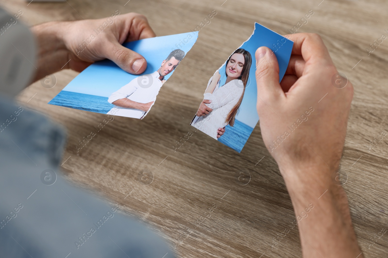 Photo of Man holding parts of photo at table indoors, closeup. Divorce concept