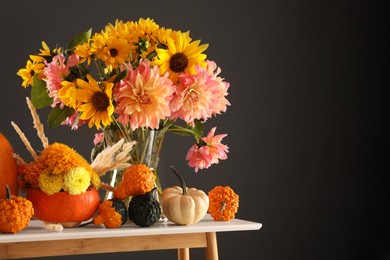 Photo of Autumn composition with beautiful flowers and pumpkins on white table against dark grey background. Space for text