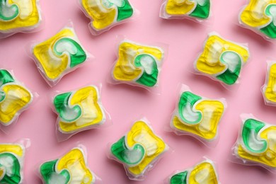Photo of Many dishwasher detergent pods on pink background, flat lay
