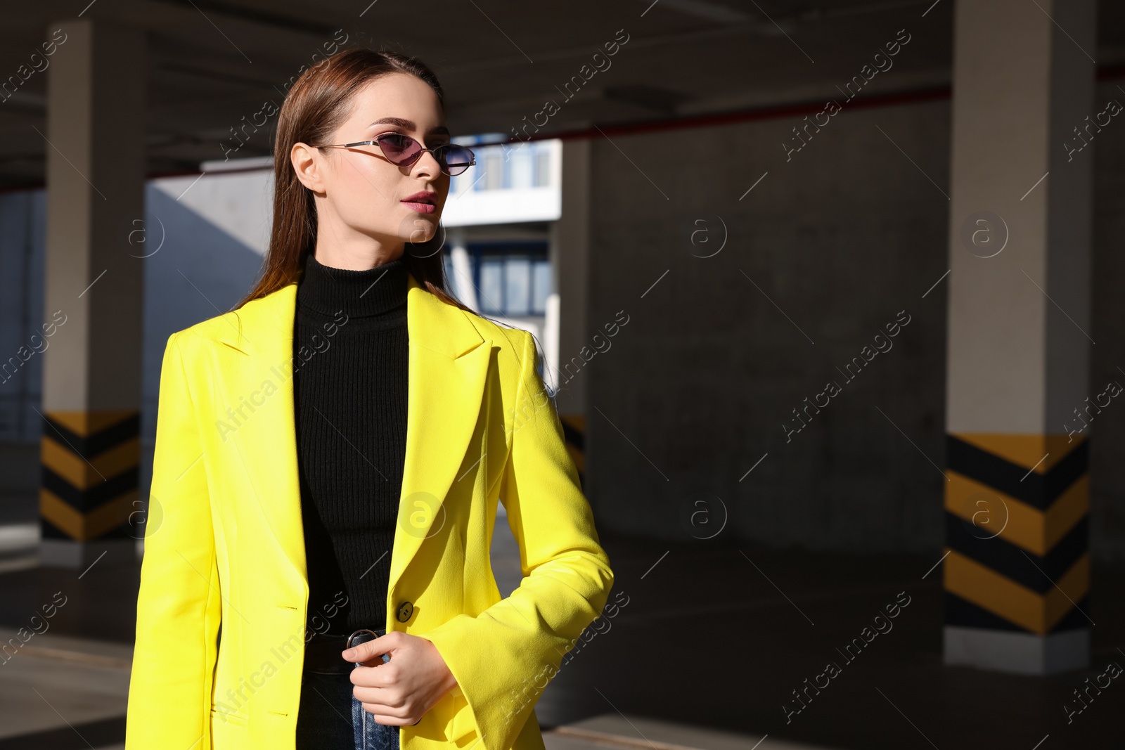 Photo of Fashionable young woman wearing stylish outfit with yellow jacket in open parking garage. Space for text