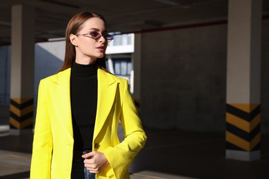 Fashionable young woman wearing stylish outfit with yellow jacket in open parking garage. Space for text