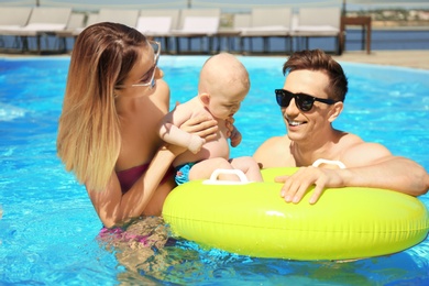 Happy parents with little baby in swimming pool on sunny day