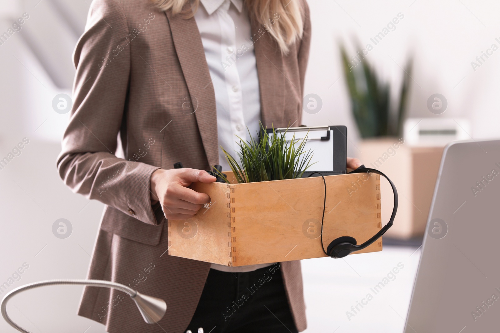 Photo of Young woman holding moving box with office stuff indoors, closeup