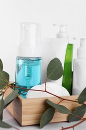 Photo of Different face cleansing products, cotton pads and eucalyptus leaves on white table