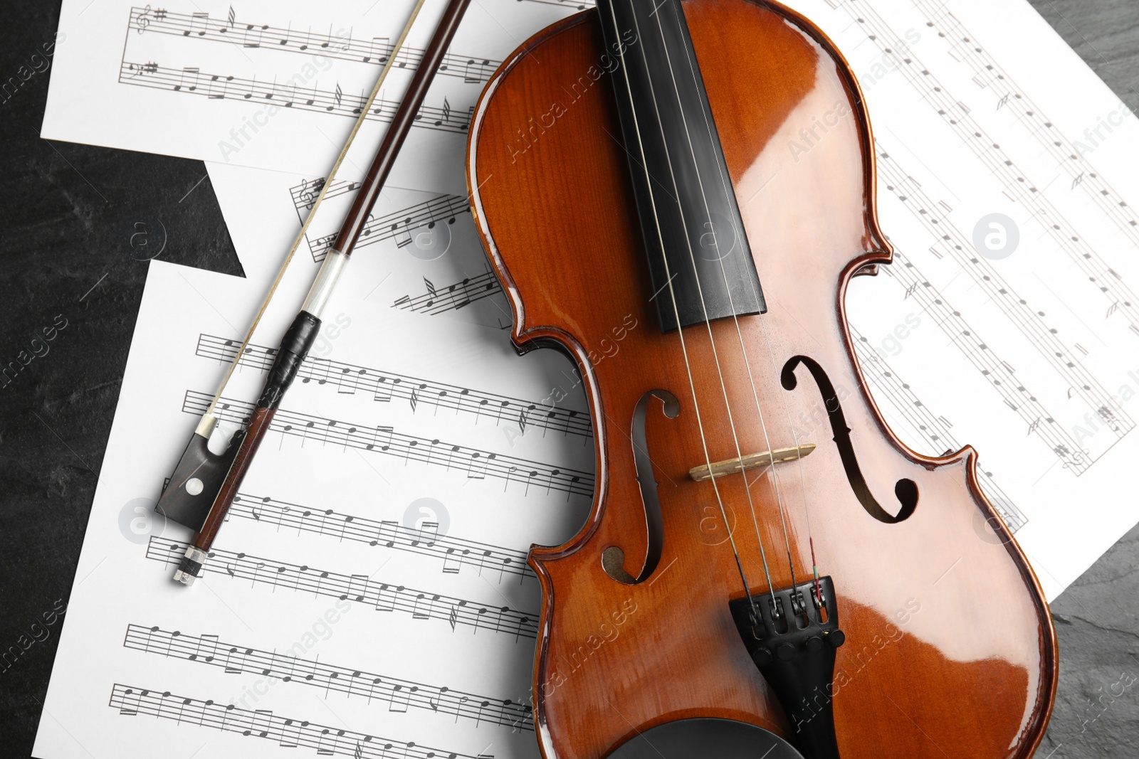 Photo of Violin, bow and note sheets on stone table, flat lay