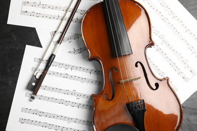 Photo of Violin, bow and note sheets on stone table, flat lay