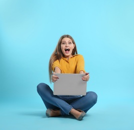 Photo of Emotional young woman with laptop celebrating victory on color background