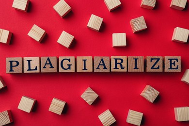 Wooden cubes with word Plagiarism on red background, flat lay