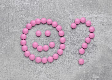 Photo of Happy emoticon with question mark made of pink antidepressants on light grey background, flat lay