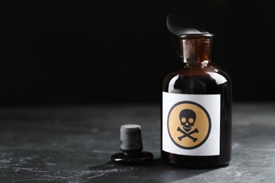 Photo of Open glass bottle of smoking poison with warning sign on black table. Space for text