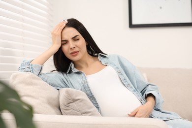 Photo of Pregnant woman suffering from headache on sofa at home