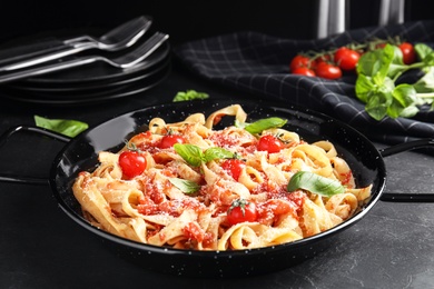 Photo of Tasty pasta with tomatoes, cheese and basil on black table