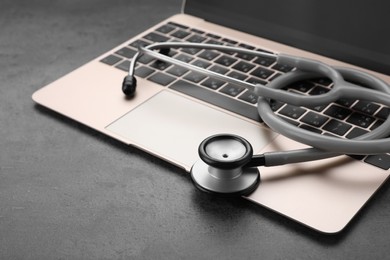 Photo of Laptop with stethoscope on grey table, closeup. Space for text