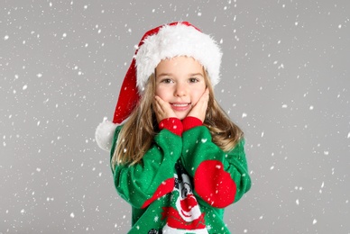 Image of Cute child in Santa hat under snowfall on grey background. Christmas celebration