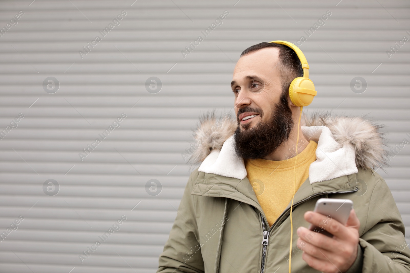 Photo of Mature man with headphones listening to music near light wall. Space for text