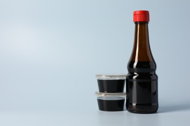 Photo of Bottle and bowls with soy sauce on light grey background, space for text