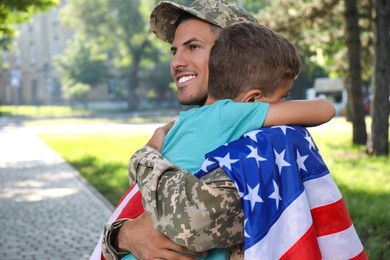 Photo of Soldier with flag of USA and his little son hugging outdoors