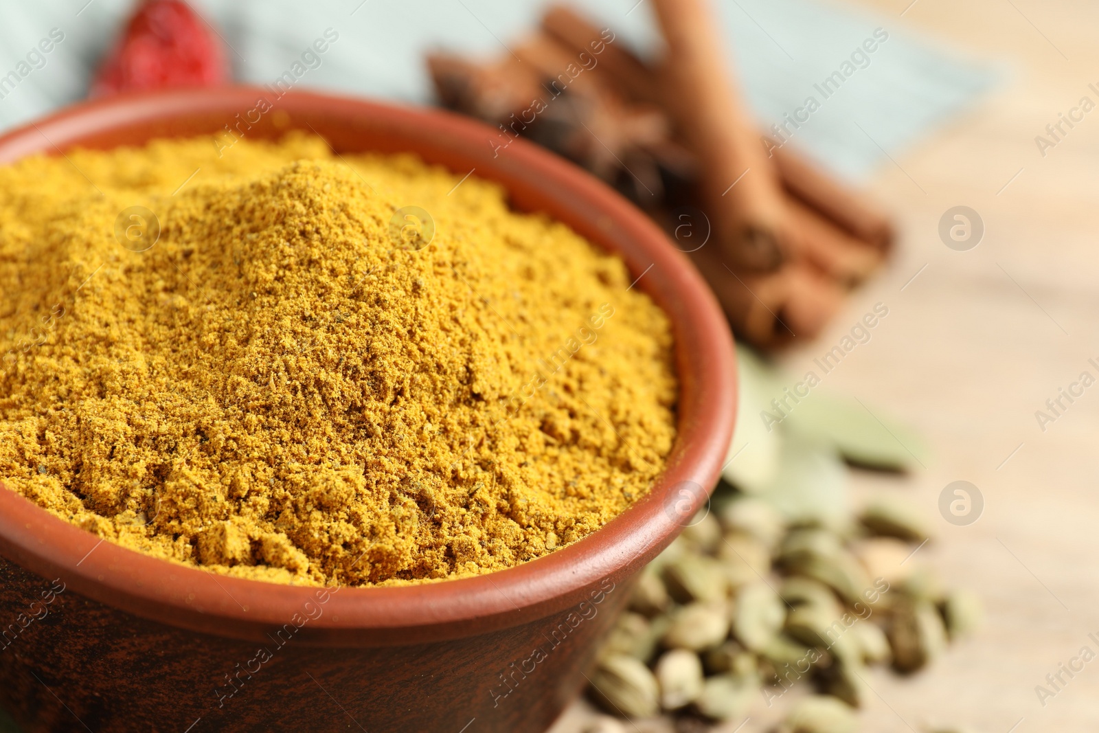 Photo of Curry powder in bowl and other spices on wooden table, closeup. Space for text