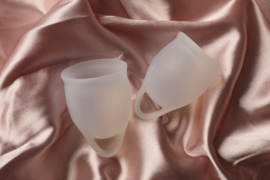 Photo of Menstrual cups on pink silk fabric, flat lay