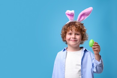 Photo of Cute boy in bunny ears headband holding Easter egg on light blue background. Space for text