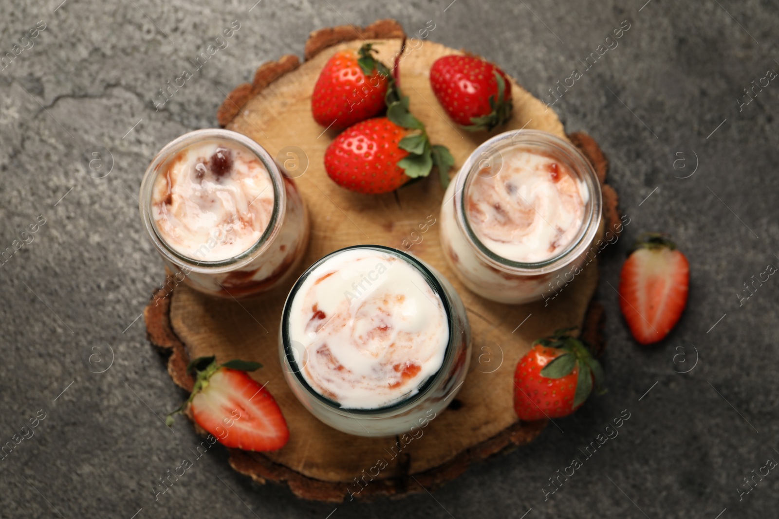 Photo of Tasty yoghurt with jam and strawberries on grey textured table, top view