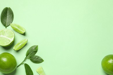 Whole and cut fresh ripe limes with leaves on light green background, flat lay