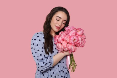 Photo of Beautiful young woman with bouquet of peonies on pink background