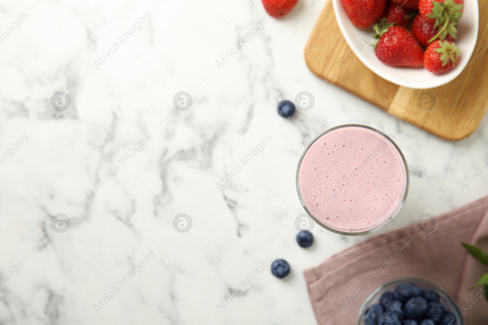 Photo of Tasty milk shake and berries on white marble table, flat lay. Space for text