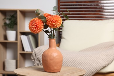 Photo of Ceramic vase with beautiful flowers on coffee table near armchair indoors