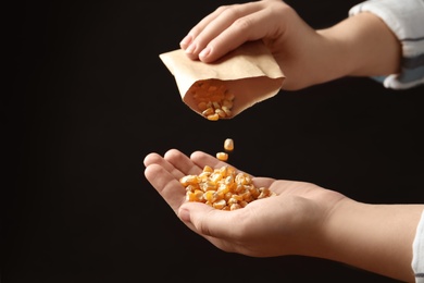 Photo of Woman pouring corn seeds from paper bag into hand on black background, closeup. Vegetable planting