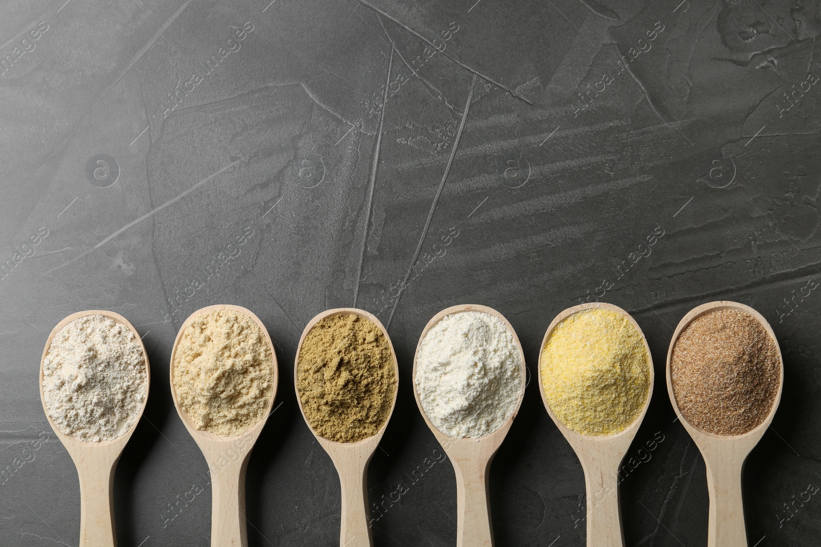 Photo of Spoons with different types of flour on grey background, top view. Space for text