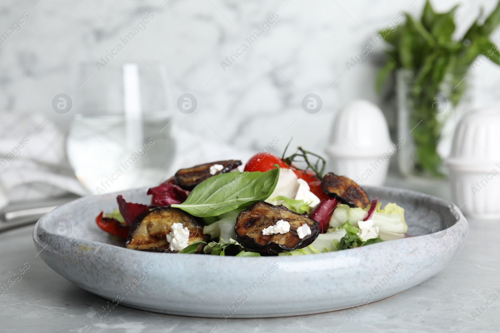 Photo of Delicious salad with roasted eggplant, basil and cheese served on grey marble table