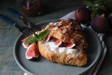 Photo of Delicious croissant with figs and cream served on light blue wooden table, closeup