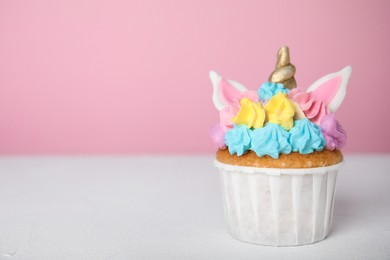 Photo of Cute sweet unicorn cupcake on white table against pink background. Space for text