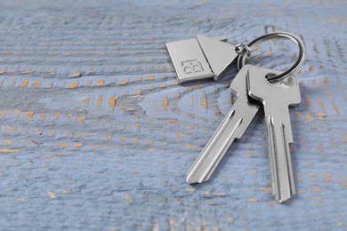 Photo of Keys with keychain in shape of house on grey wooden table, closeup. Space for text