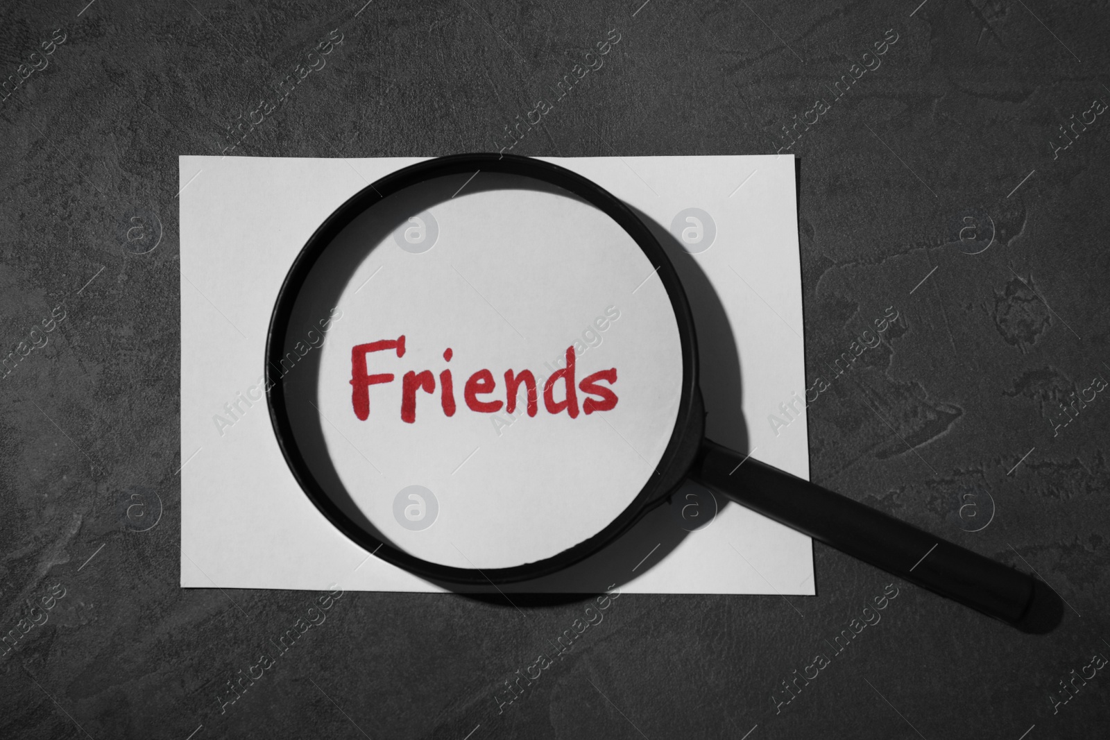 Photo of Magnifying glass and sheet of paper with word FRIENDS on grey background, flat lay. Loneliness concept