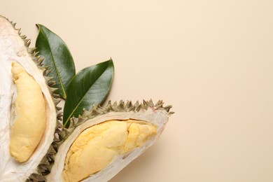 Photo of Piecesfresh ripe durian and leaves on beige background, flat lay. Space for text