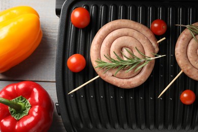 Photo of Electric grill with homemade sausages, rosemary and vegetables on rustic wooden table, flat lay