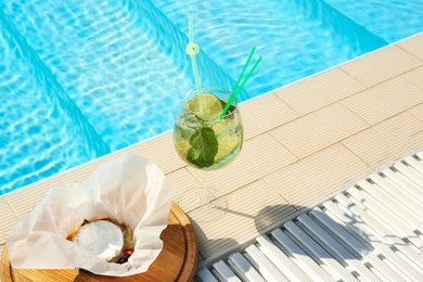 Photo of Glass of delicious mojito and brie cheese near swimming pool. Refreshing drink