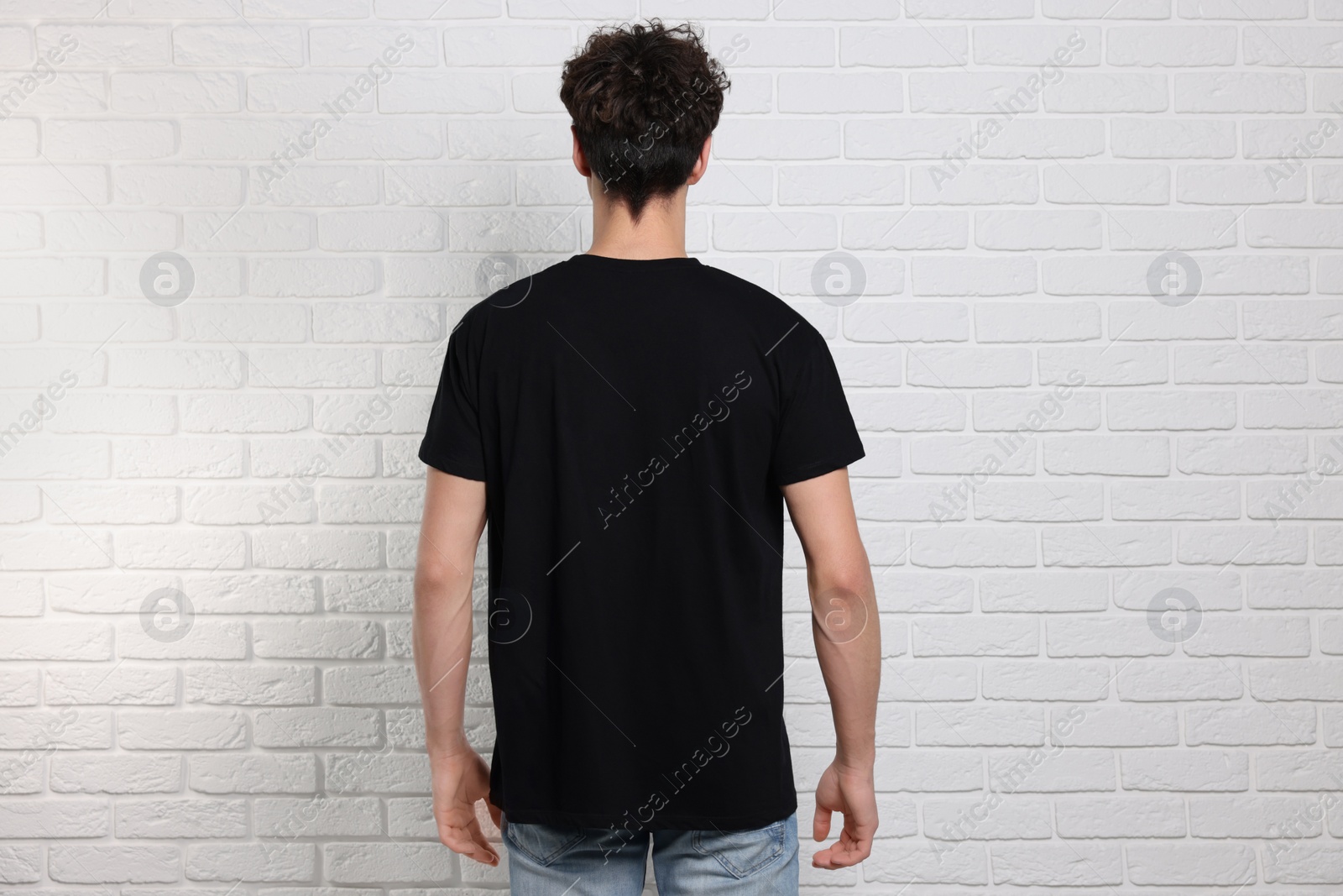 Photo of Man wearing black t-shirt near white brick wall, back view. Mockup for design