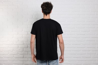 Man wearing black t-shirt near white brick wall, back view. Mockup for design