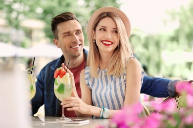 Young couple with glasses of tasty lemonade in open-air cafe