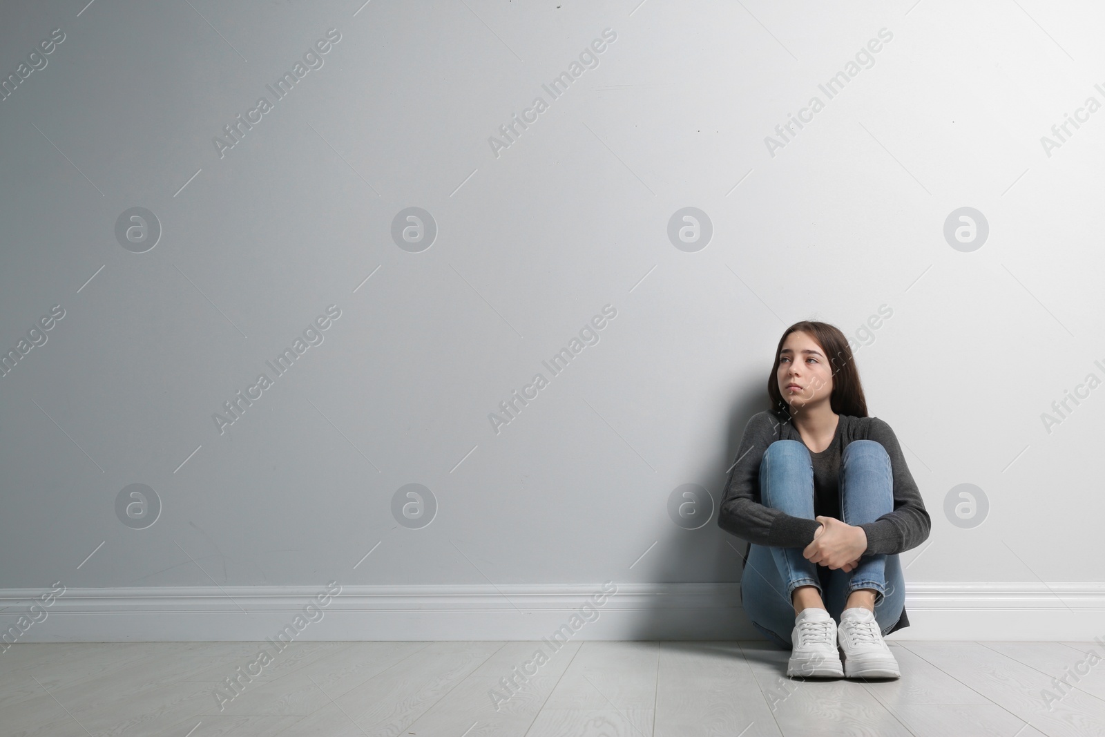 Photo of Upset teenage girl sitting on floor near wall. Space for text